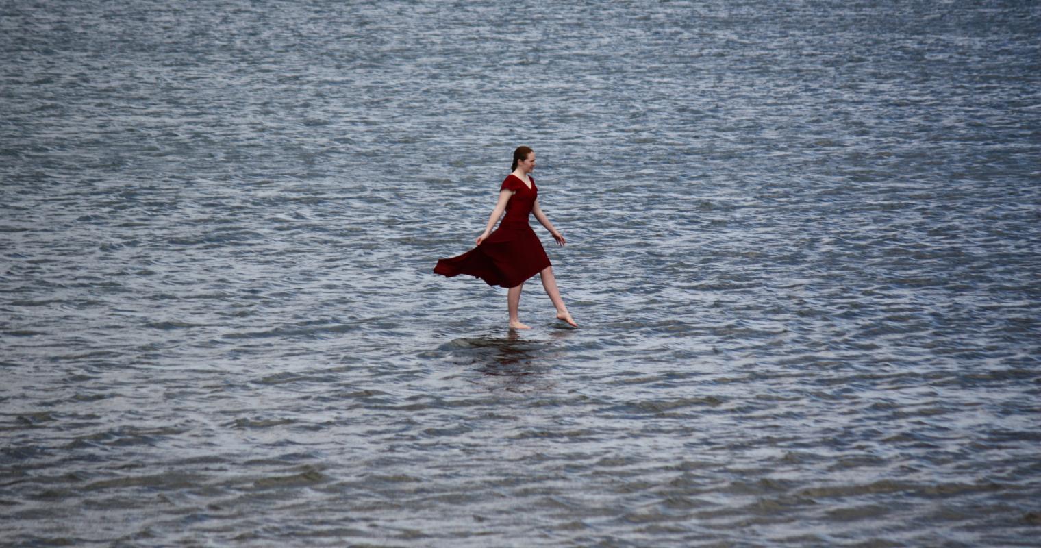 image of woman in dress walking through water