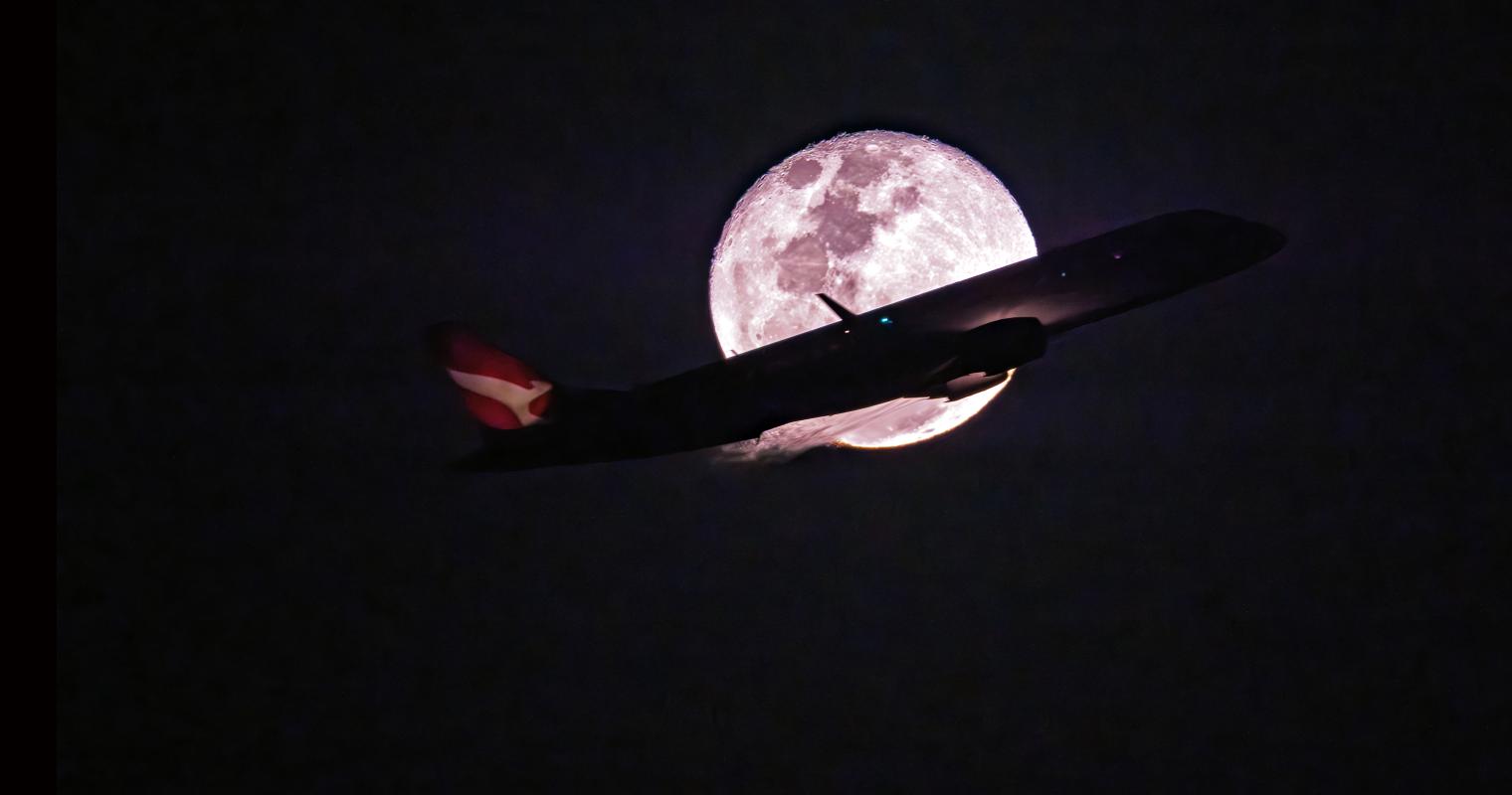 image of a plane flying in front of the moon at night