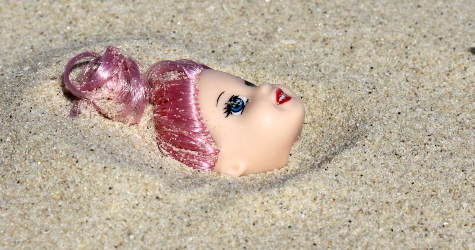 image of a barbie face protruding from the sand
